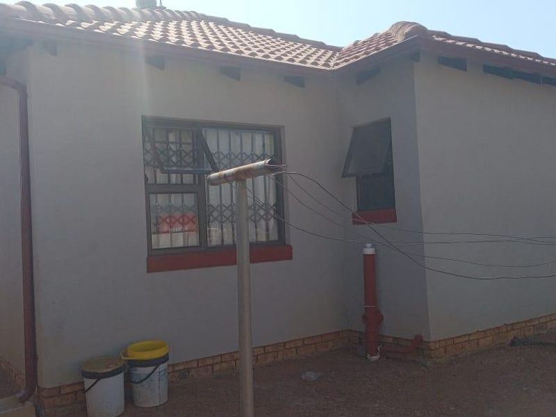 Rear exterior view of a single-story house featuring a tiled roof, painted masonry walls, and security-fitted windows.