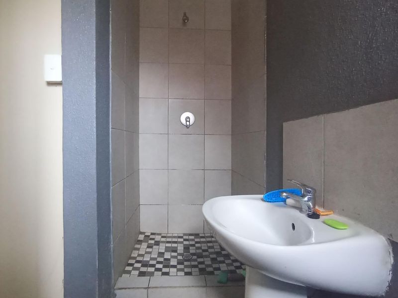 A compact bathroom featuring a pedestal basin and a tiled shower enclosure with mosaic flooring, requiring some finishing touches to the wall tiling.