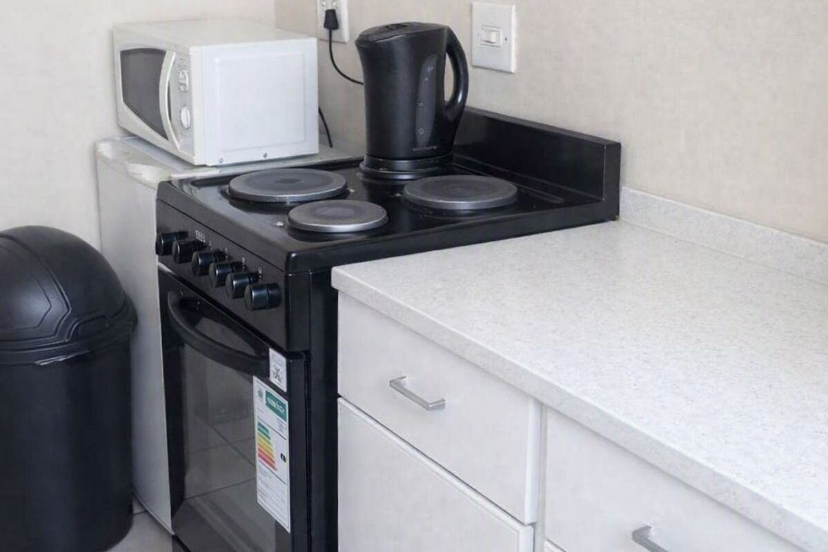 A compact kitchen area featuring white cabinetry, a laminate countertop, and a freestanding electric stove with ceramic tiled flooring.