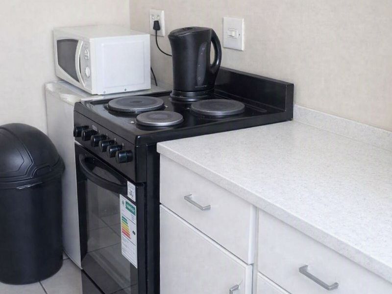 A compact kitchen area featuring white cabinetry, a laminate countertop, and a freestanding electric stove with ceramic tiled flooring.