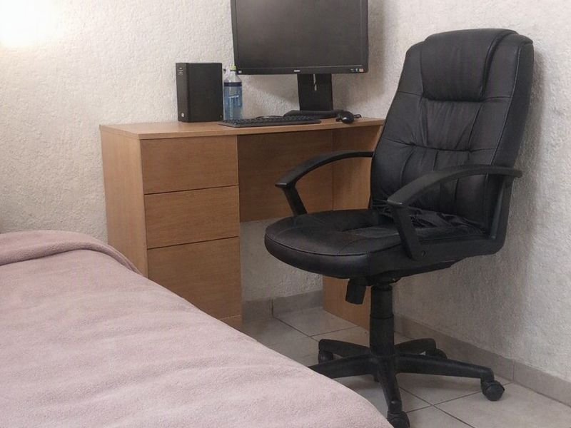 A bedroom featuring tiled flooring and textured wall finishes, currently set up with a workspace area.