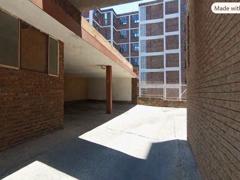 A covered parking area featuring brick construction and concrete flooring, situated within an apartment complex.