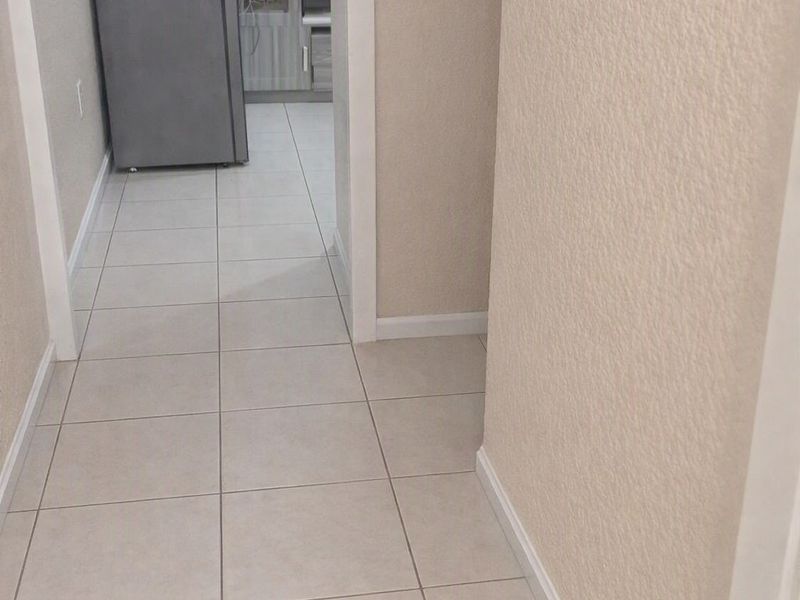 A neutral-toned hallway featuring tiled flooring and clean white trim, leading into an adjacent living area.