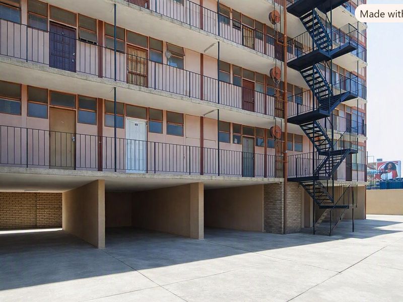 Exterior view of an apartment building featuring an external metal staircase, concrete parking area, and multi-level balcony access.