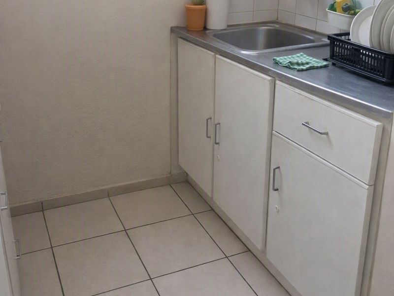 A functional scullery or utility area featuring a stainless steel sink, built-in white cabinetry, and tiled flooring.