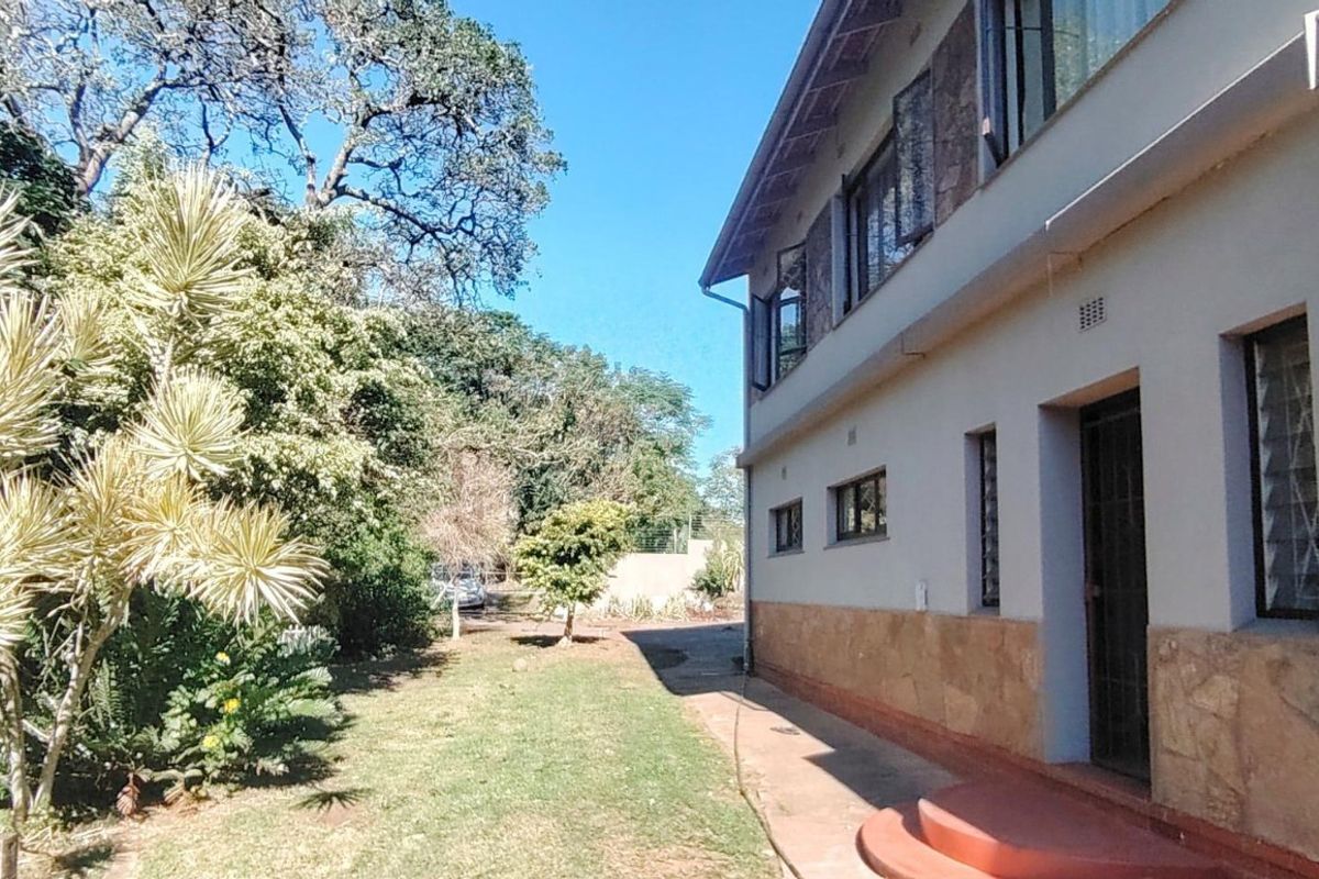 A view of the rear exterior of the house featuring stone cladding, louvre windows, and a concrete pathway leading along the garden.