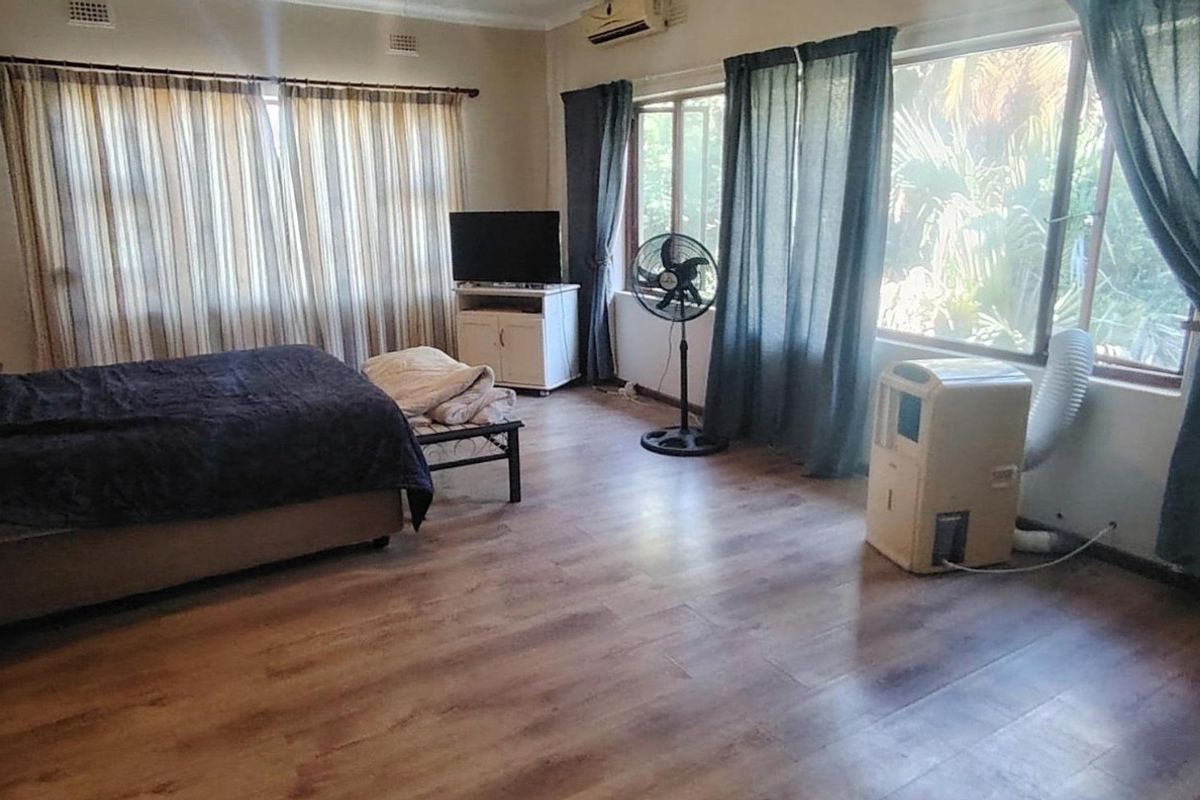 Spacious bedroom featuring laminate flooring, large windows allowing natural light, and a wall-mounted air conditioning unit.