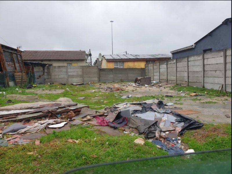 A vacant residential plot enclosed by precast concrete boundary walls, currently requiring significant site clearance and debris removal.