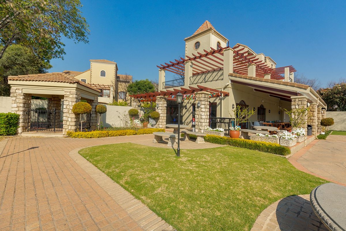 A well-maintained rear exterior featuring a stone-clad facade, timber pergola, covered patio area, and landscaped garden with paved walkways.