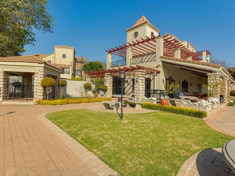 A well-maintained rear exterior featuring a stone-clad facade, timber pergola, covered patio area, and landscaped garden with paved walkways.