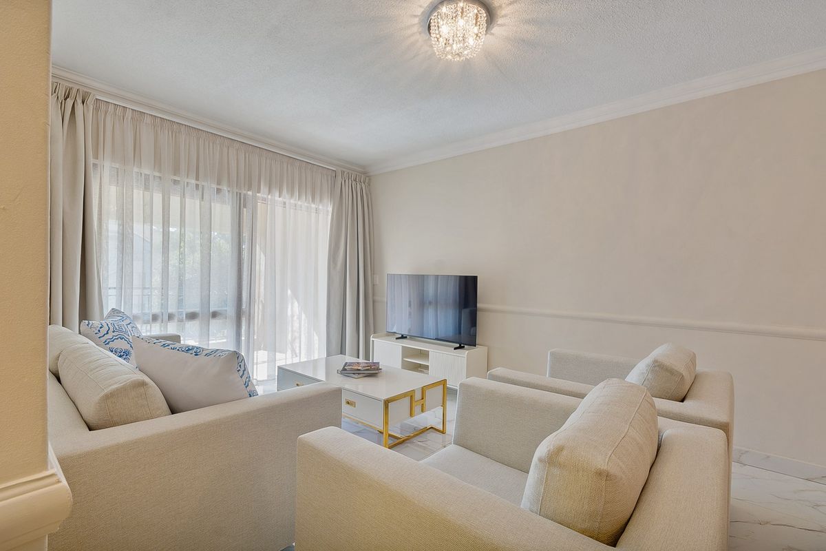 A bright and well-maintained living room featuring tiled flooring, crown molding, chair rail detailing, and a large sliding glass door providing natural light.