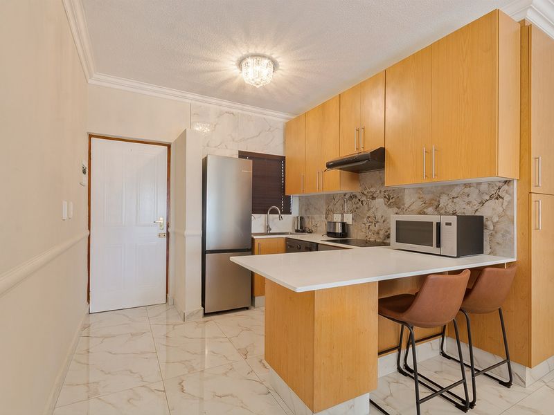 Compact kitchen featuring light wood cabinetry, stone countertops, a breakfast bar, and modern marble-look tiling throughout.