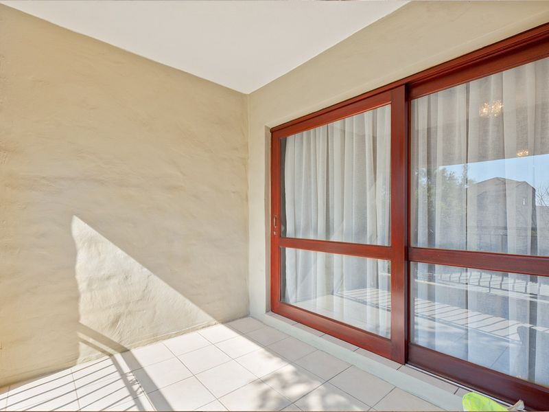 A covered balcony featuring tiled flooring and a large wooden-framed sliding glass door providing access to the interior.