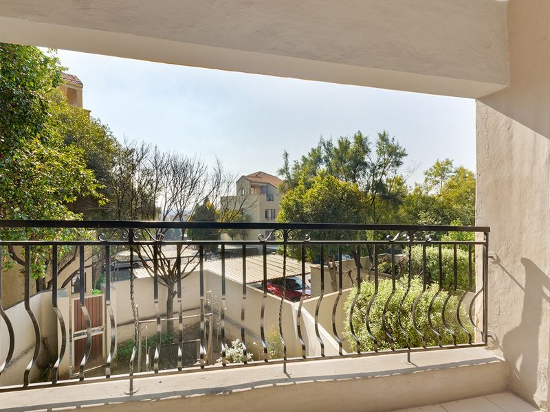 A covered balcony featuring a decorative wrought iron balustrade and tiled flooring, offering an elevated view of the surrounding residential area.