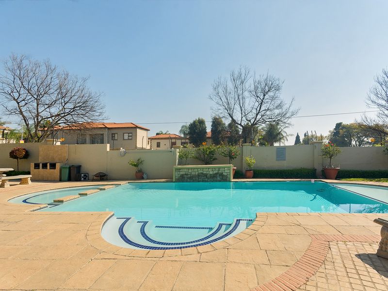 A communal outdoor pool area featuring a paved deck, built-in braai facility, and perimeter walling, providing a functional space for recreation and leisure.