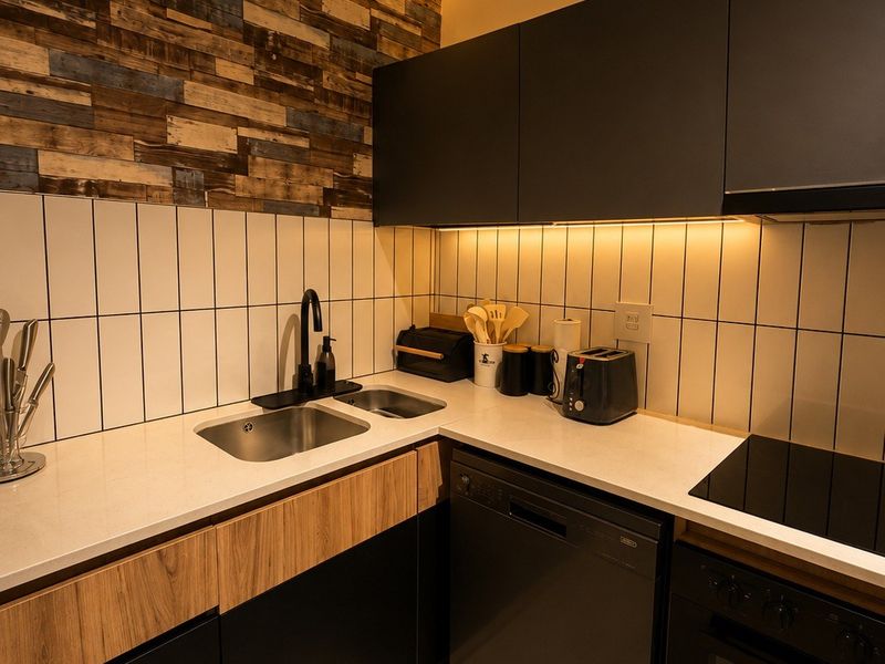 Modern kitchen featuring sleek matte cabinetry, stone countertops, integrated appliances, and a distinctive slatted timber ceiling with ambient LED lighting.