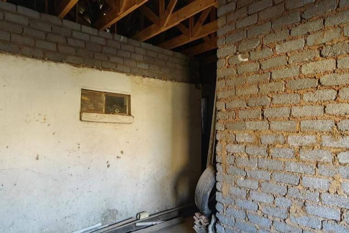 An unfinished utility space featuring exposed brickwork, exposed timber roof trusses, and plastered wall sections, offering potential for renovation or storage conversion.