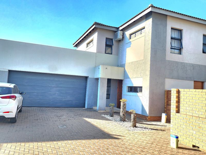 Front elevation of a double-story cluster home featuring a double garage, paved driveway, and brick boundary walling.