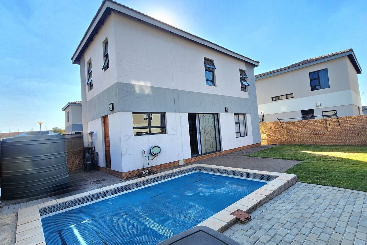 Rear exterior view of a double-story cluster home featuring a swimming pool with cover, paved patio area, lawn, and a large water storage tank.