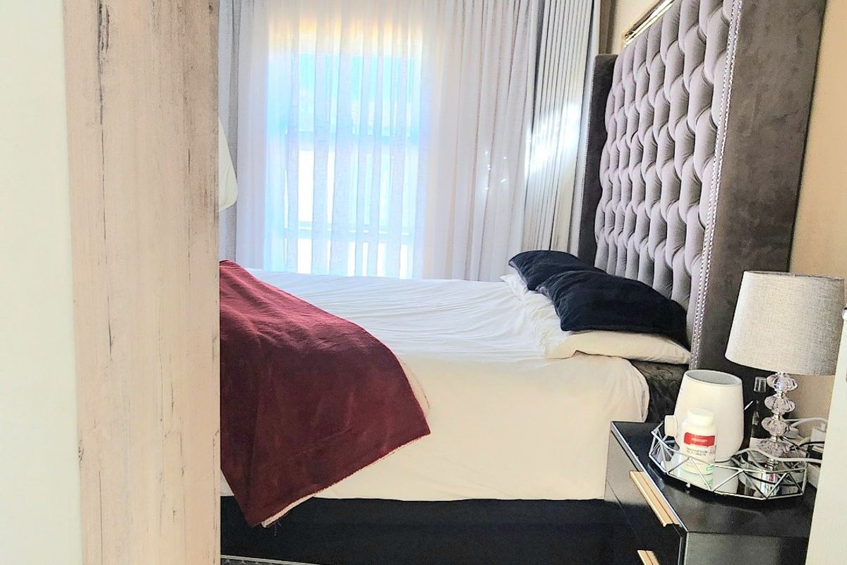 A well-maintained bedroom featuring neutral tiled flooring, a ceiling light fixture, and large windows dressed with elegant curtains.