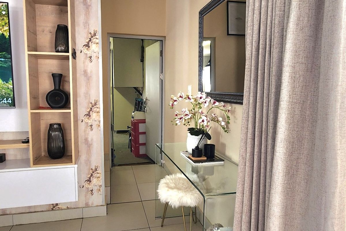 A living area featuring tiled flooring, coved ceilings, and a built-in shelving unit with decorative wallpaper accents.
