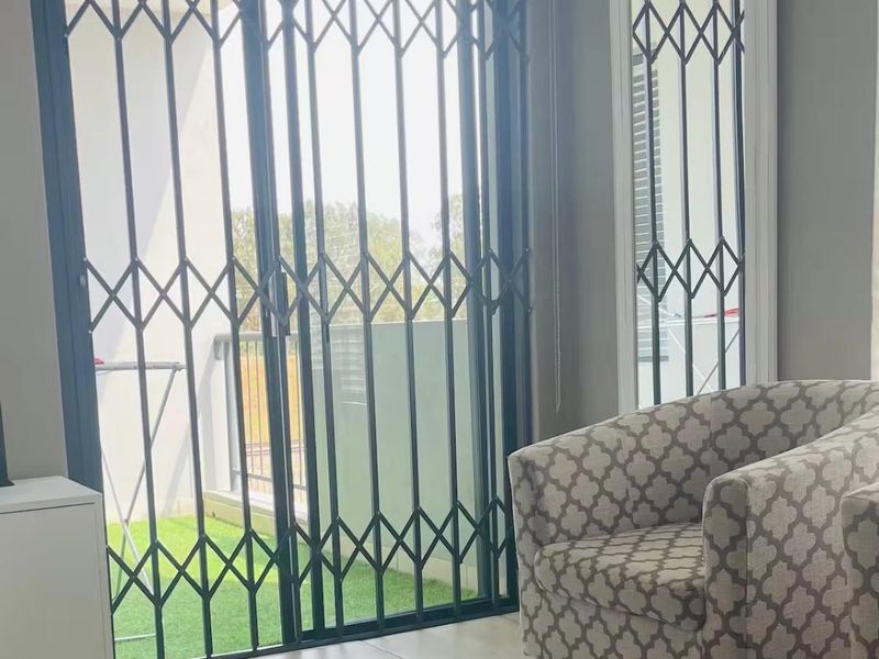 A living room area featuring tiled flooring, a sliding glass door with a security gate, and access to an outdoor balcony space.