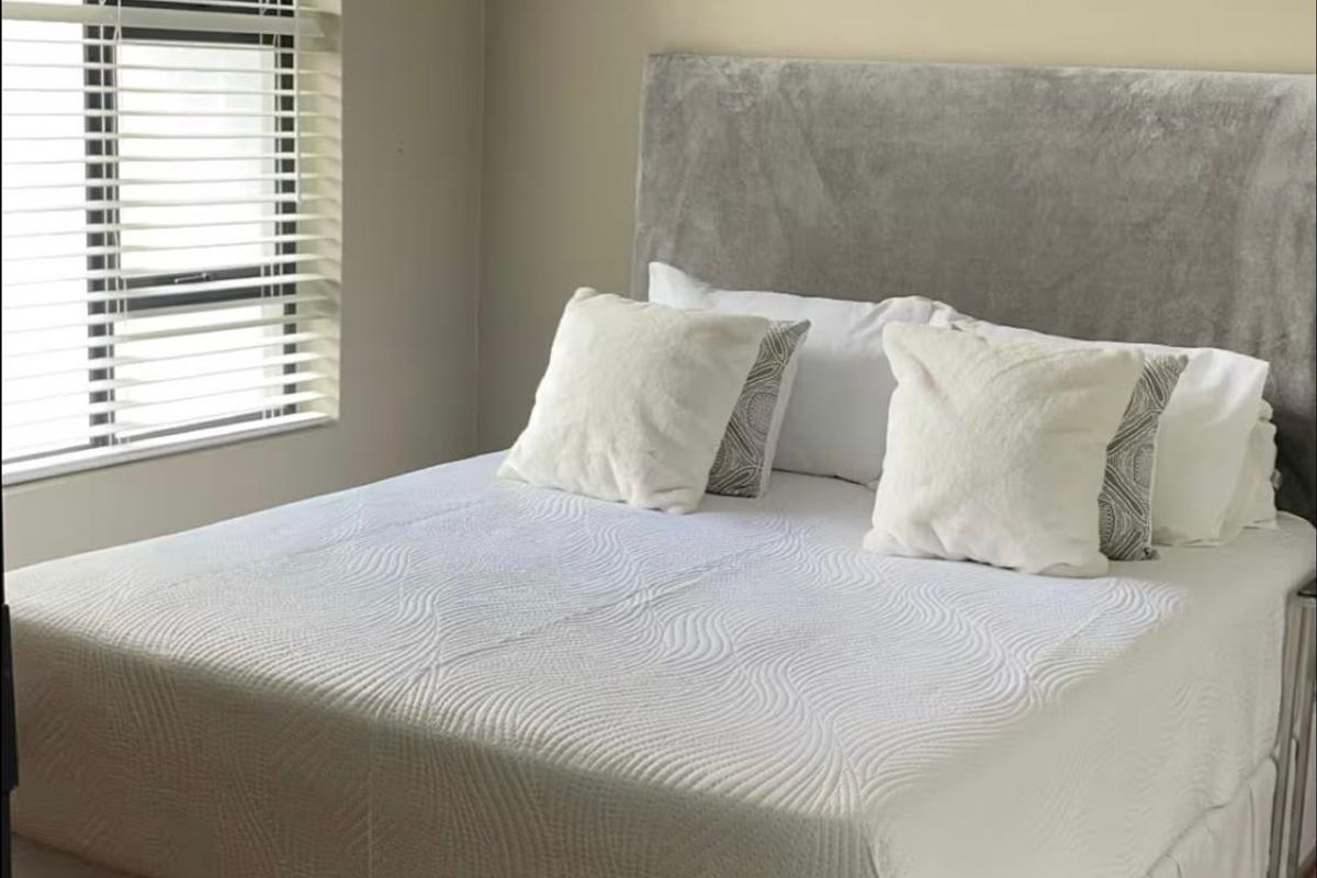 A well-lit bedroom featuring laminate flooring and venetian blinds, providing a clean and neutral space.
