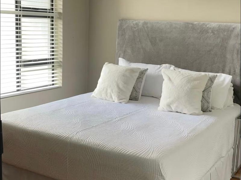 A well-lit bedroom featuring laminate flooring and venetian blinds, providing a clean and neutral space.