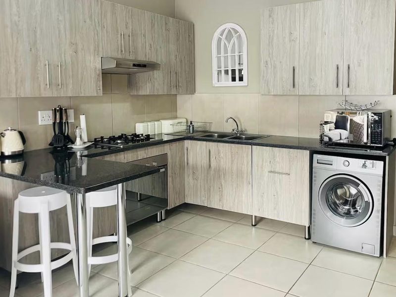 Modern kitchen featuring light wood-grain cabinetry, dark granite countertops, a gas hob, built-in oven, and integrated laundry plumbing.