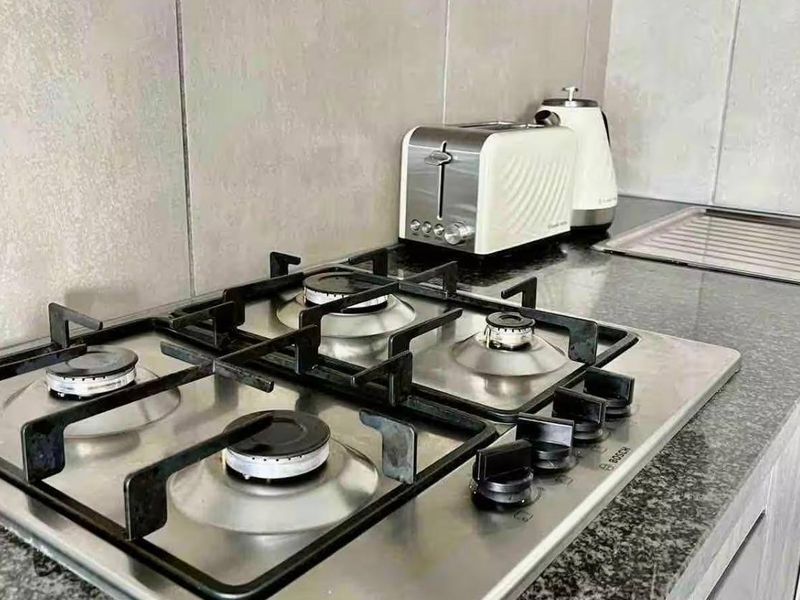 Modern kitchen featuring a stainless steel gas hob, granite countertops, and neutral tiled backsplash with built-in cabinetry.