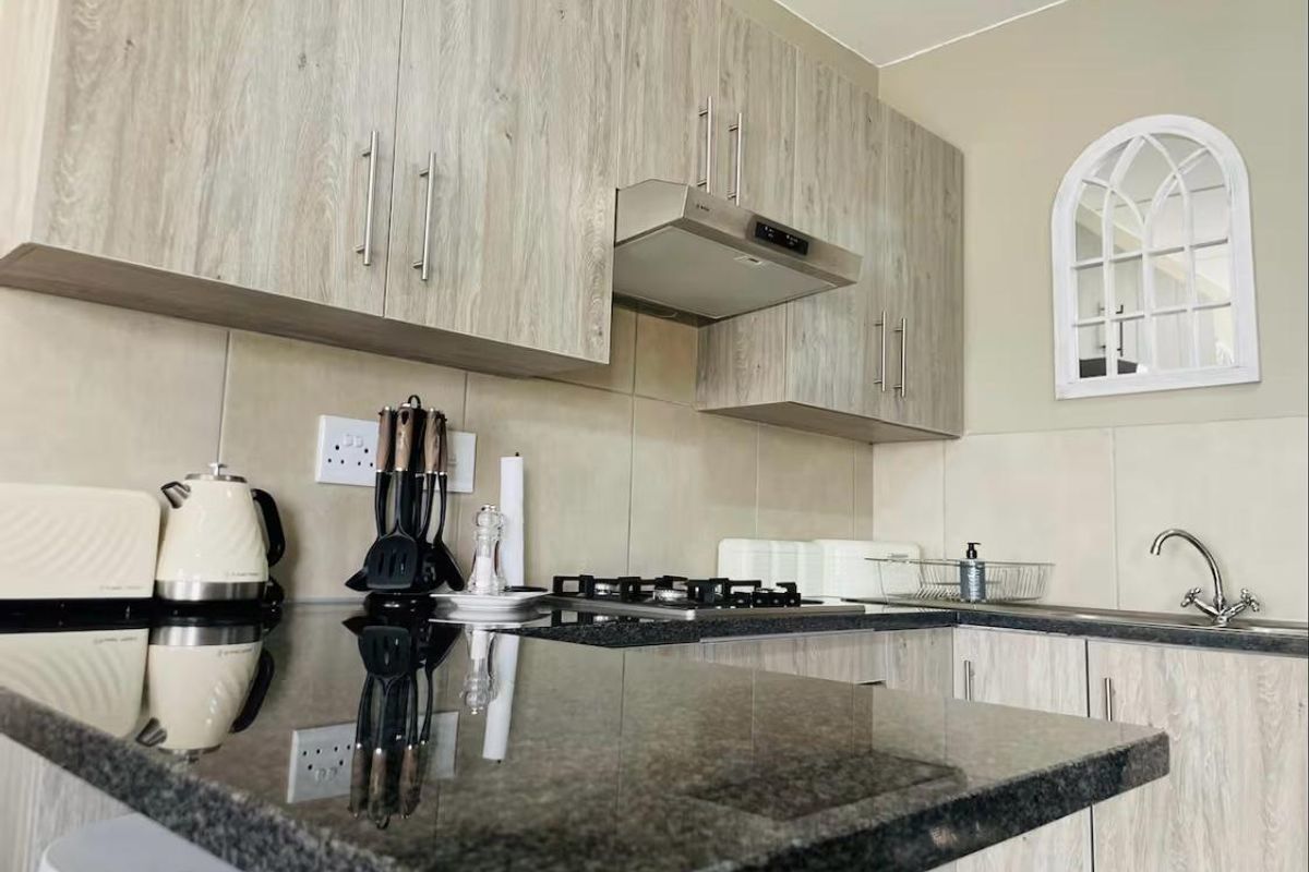Modern kitchen featuring light wood-grain cabinetry, dark granite countertops, a gas hob with extractor fan, and a tiled backsplash.