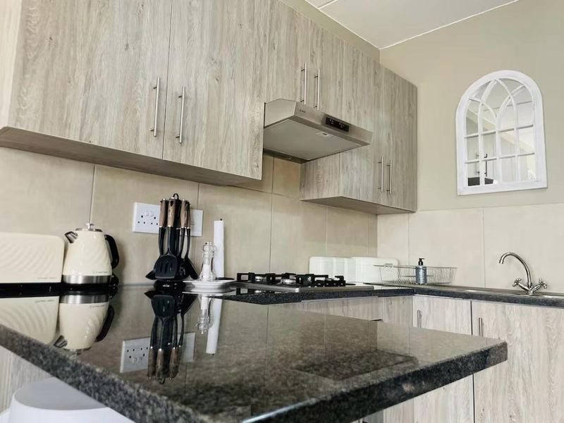 Modern kitchen featuring light wood-grain cabinetry, dark granite countertops, a gas hob with extractor fan, and a tiled backsplash.