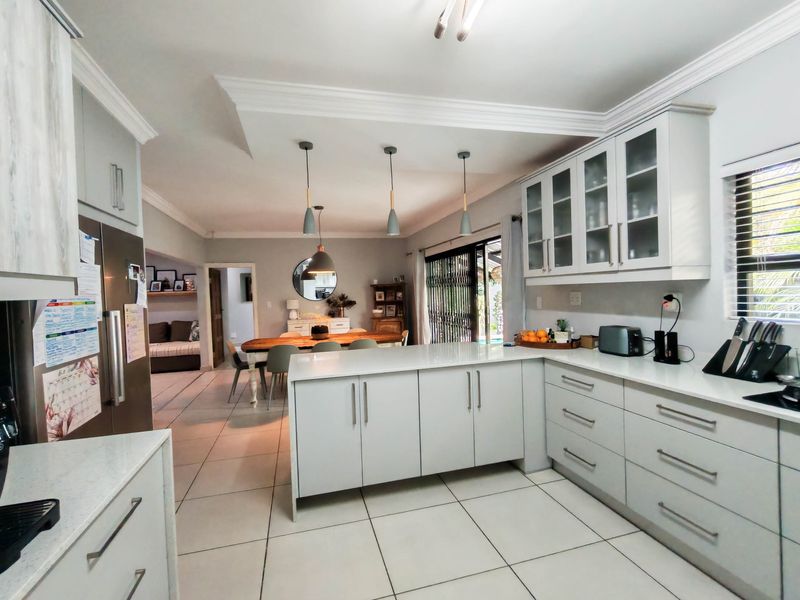A bright open-plan kitchen and dining area featuring modern cabinetry, quartz countertops, a central island, and tiled flooring with seamless flow to the outdoors.