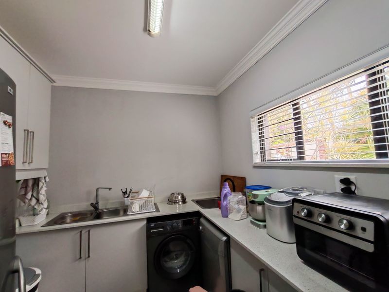 A functional laundry room featuring built-in cabinetry, a stainless steel sink, and ample counter space with a window for natural light.