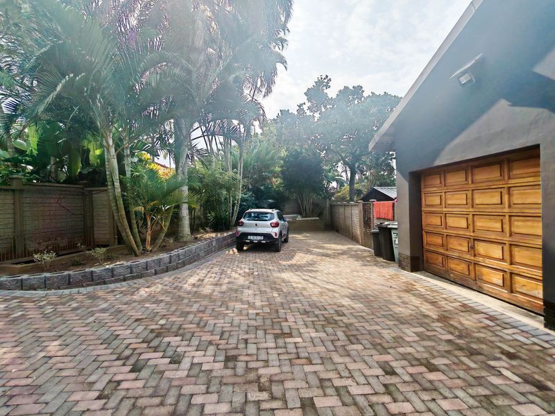 A paved driveway leading to a wooden garage door, featuring a retaining wall and established garden landscaping.