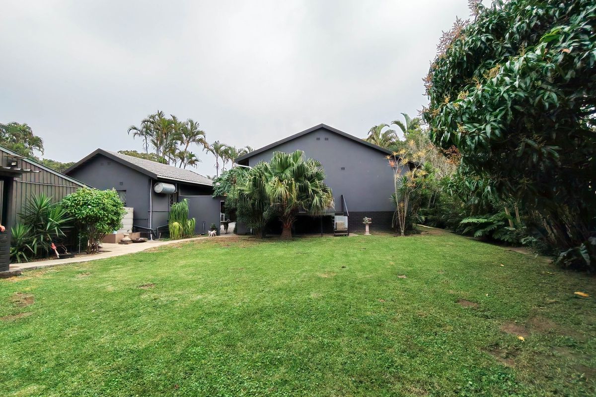 A spacious rear garden featuring a well-maintained lawn, mature landscaping, and a paved walkway leading to the rear elevation of the house.