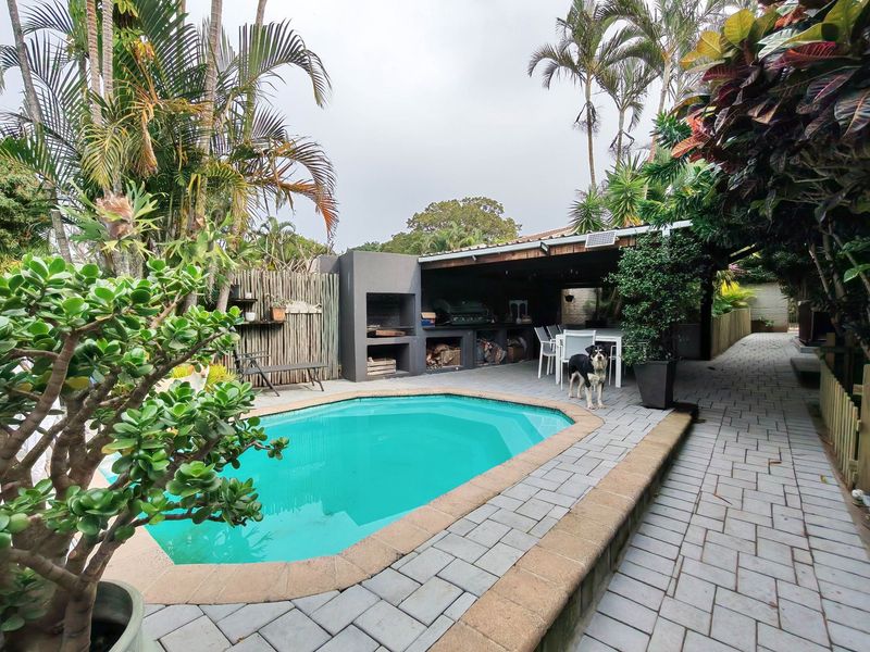 Outdoor entertainment area featuring a swimming pool, paved deck, and a covered patio with a built-in braai facility.