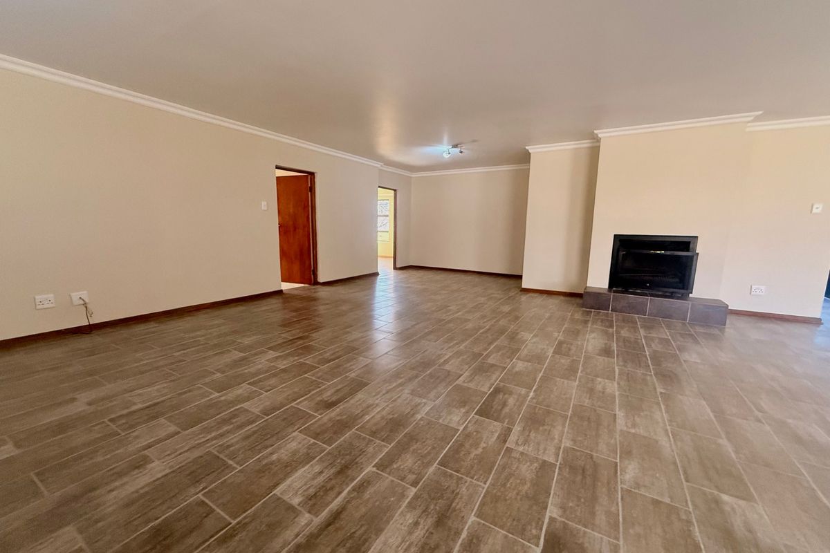 Spacious, empty living room featuring neutral walls, modern wood-look tiled flooring, and a built-in fireplace with a tiled hearth.