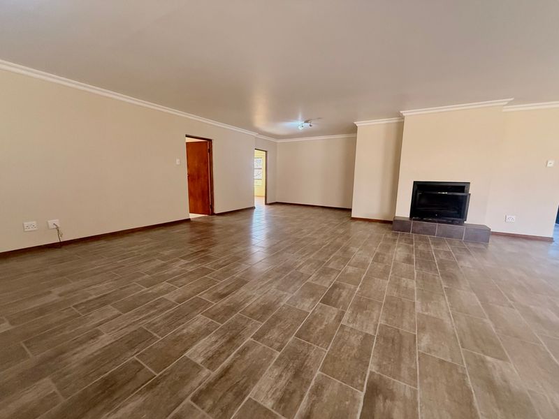 Spacious, empty living room featuring neutral walls, modern wood-look tiled flooring, and a built-in fireplace with a tiled hearth.