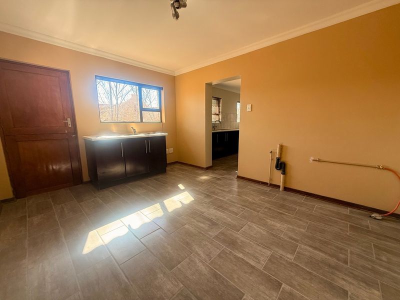 A functional laundry room featuring tiled flooring, a sink with base cabinetry, and exposed plumbing connections for appliances.