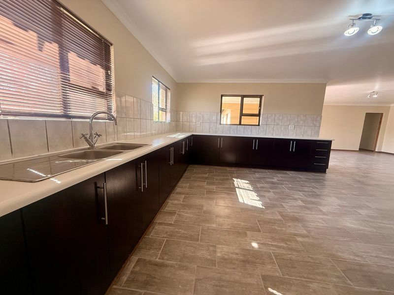 Spacious kitchen featuring dark wood cabinetry, white countertops, double sink, and neutral ceramic floor tiles, offering a clean and functional layout.