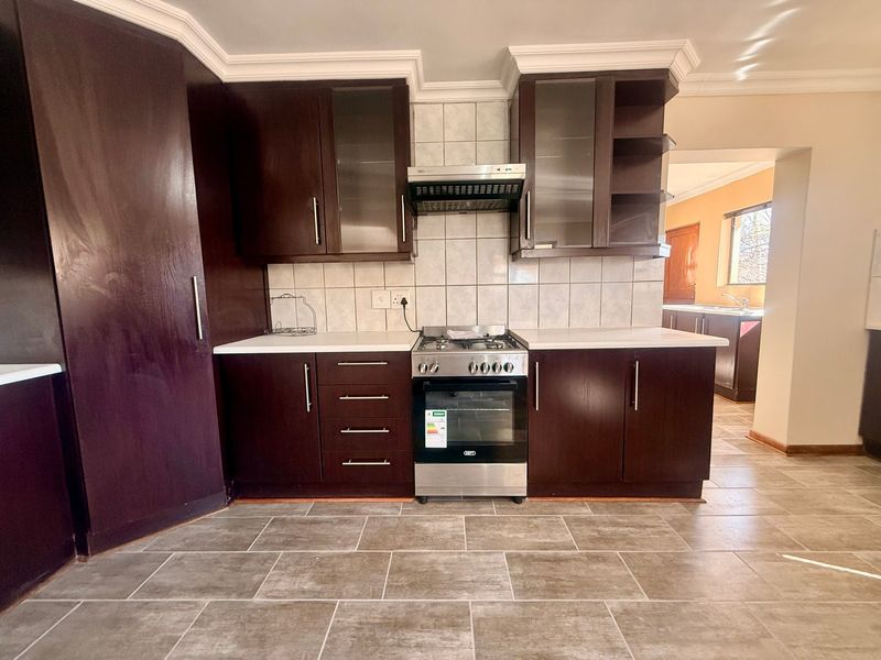 A clean, functional kitchen featuring dark wood cabinetry, stainless steel appliances, stone countertops, and neutral tiled flooring with a view into an adjacent space.