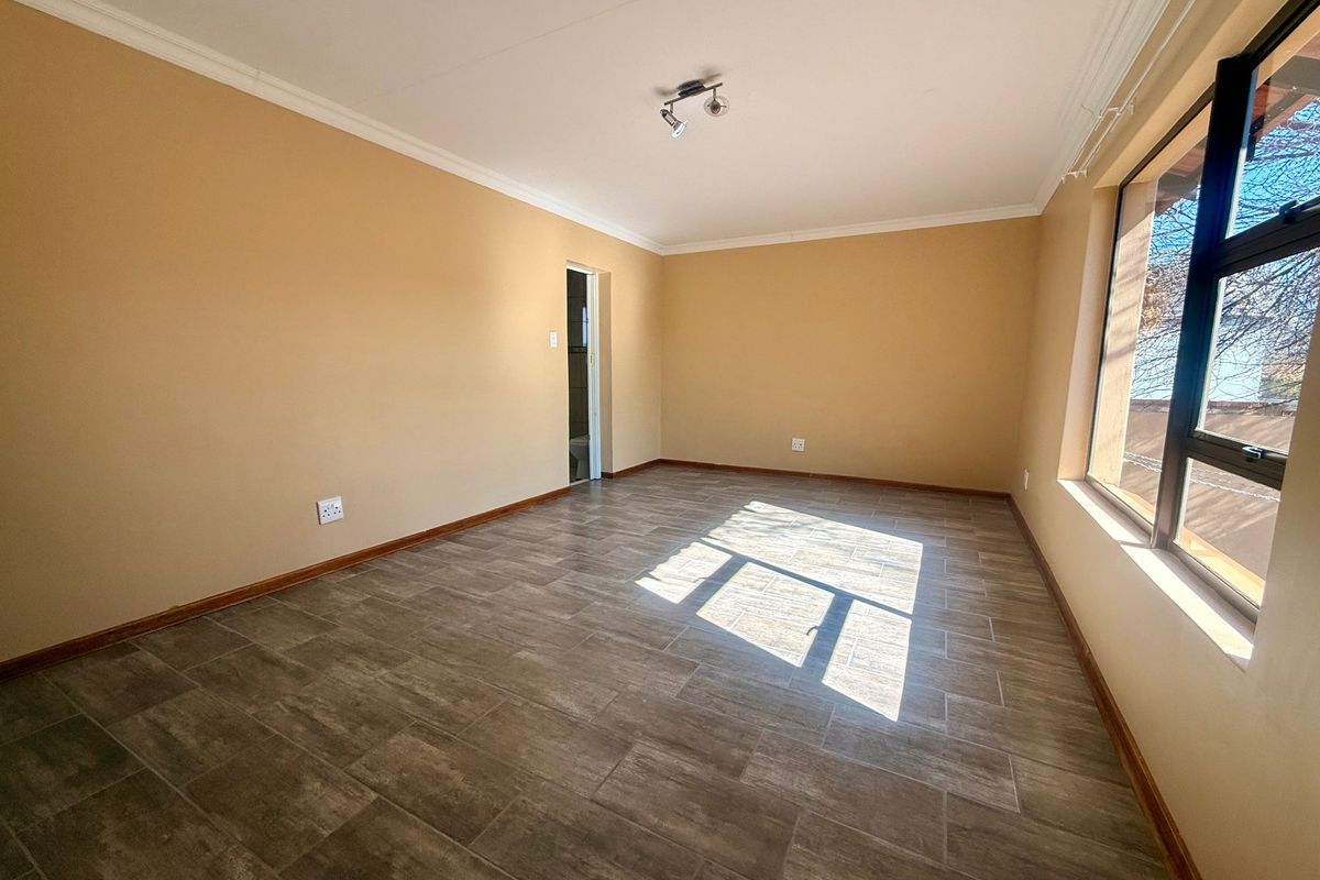 A bright, empty bedroom featuring modern tiled flooring, neutral wall paint, and large aluminium-framed windows allowing for ample natural light.
