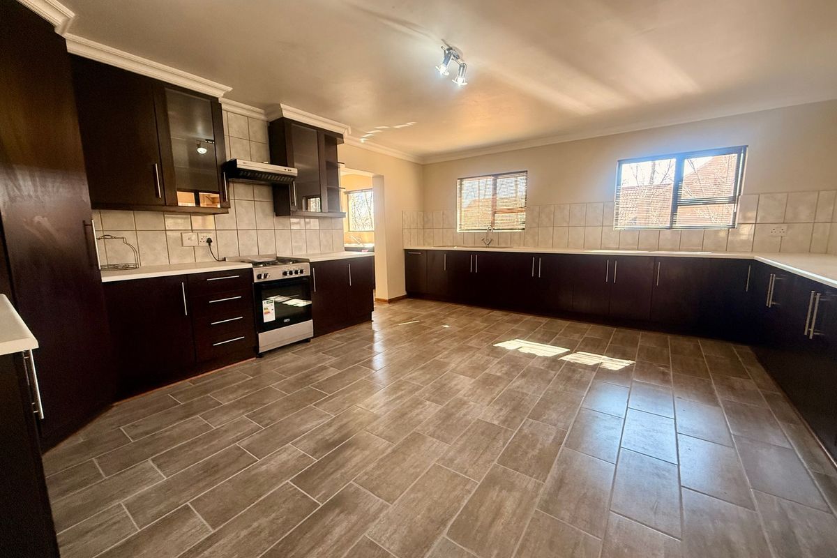 Spacious kitchen featuring dark wood cabinetry, tiled flooring, a tiled backsplash, and a freestanding oven with an extractor fan.