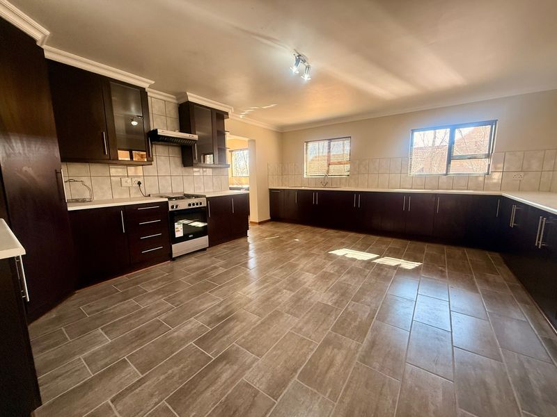 Spacious kitchen featuring dark wood cabinetry, tiled flooring, a tiled backsplash, and a freestanding oven with an extractor fan.