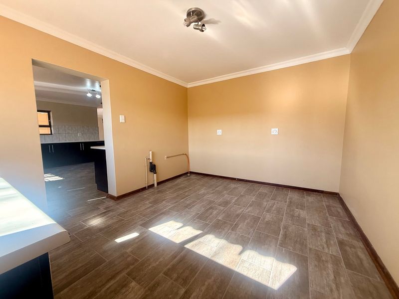 A clean, empty laundry room featuring tiled flooring, plumbing connections for appliances, and a neutral color palette, with direct access to the kitchen area.