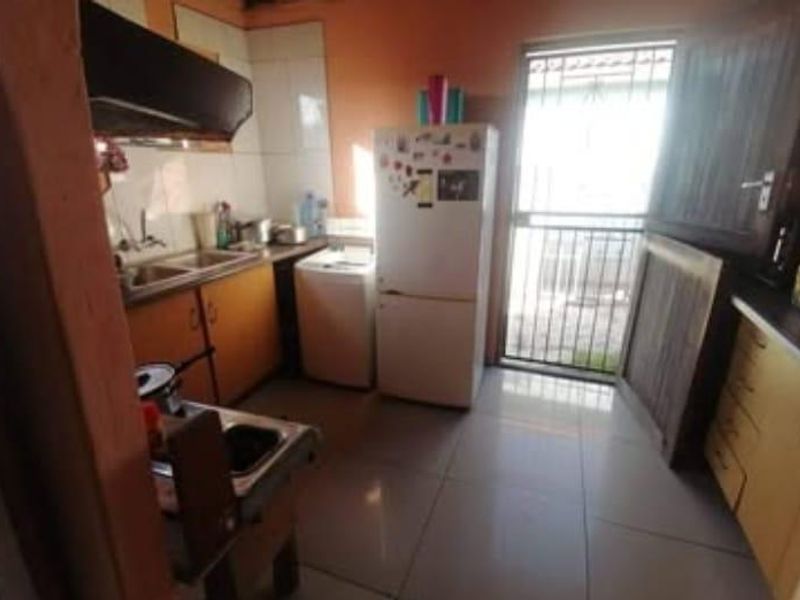 A functional kitchen featuring built-in cabinetry, a double sink, and an extractor fan, with direct access to an exterior security gate.