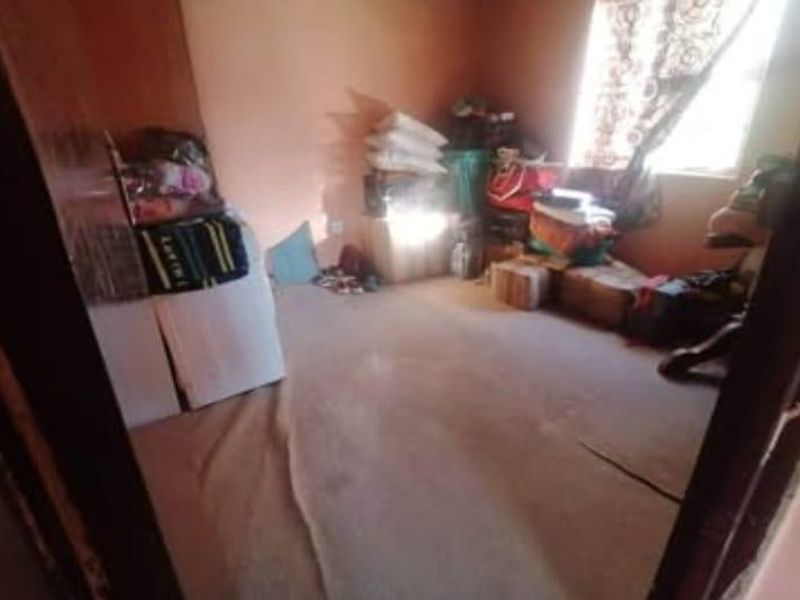 A small bedroom space featuring carpeted flooring and a window, currently used for storage.