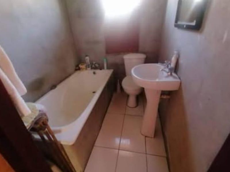 A small bathroom featuring a bathtub, pedestal basin, and toilet, currently requiring wall finishing and cosmetic updates to improve the overall condition.
