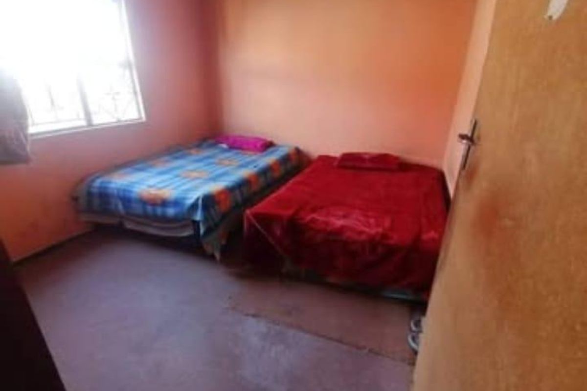 A basic bedroom featuring a window with security bars and plain wall finishes, requiring cosmetic updates to improve its overall condition.